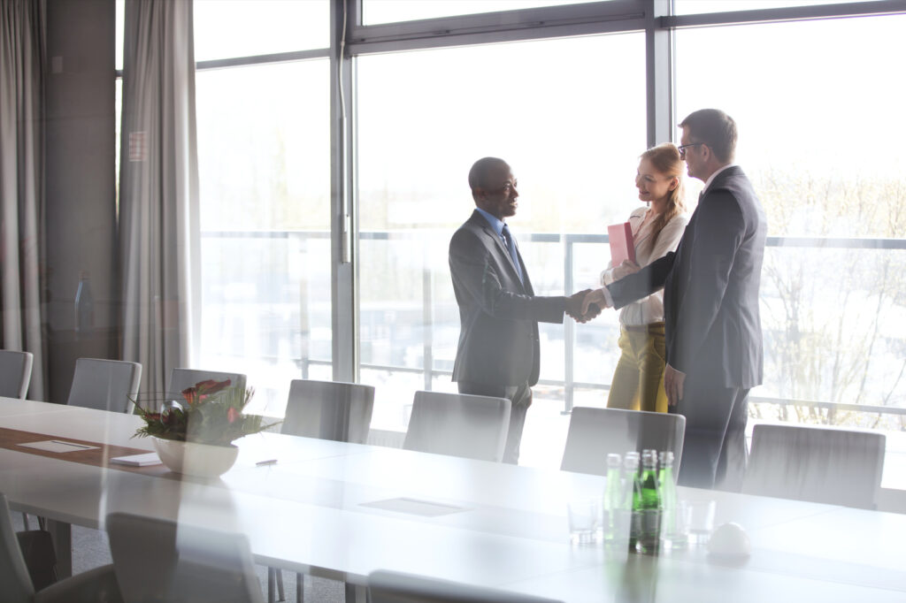 Businessmen shaking hands by female colleague in conference room at office